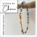 Load image into Gallery viewer, Beaded necklace with gold, blue, and brown beads on a wooden stick against a light background.