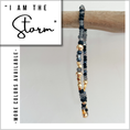 Load image into Gallery viewer, Beaded bracelet with gold and black beads on a wooden stick, with text 'I AM THE Storm' and 'More colors available'.