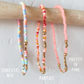 Load image into Gallery viewer, Three beaded necklaces labeled 'Confetti Mix', 'Parfait', and 'Pretty in Pink' on a wooden stick.