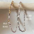 Load image into Gallery viewer, Two beaded bracelets, one with gold beads and the other with silver beads, on a wooden stick.