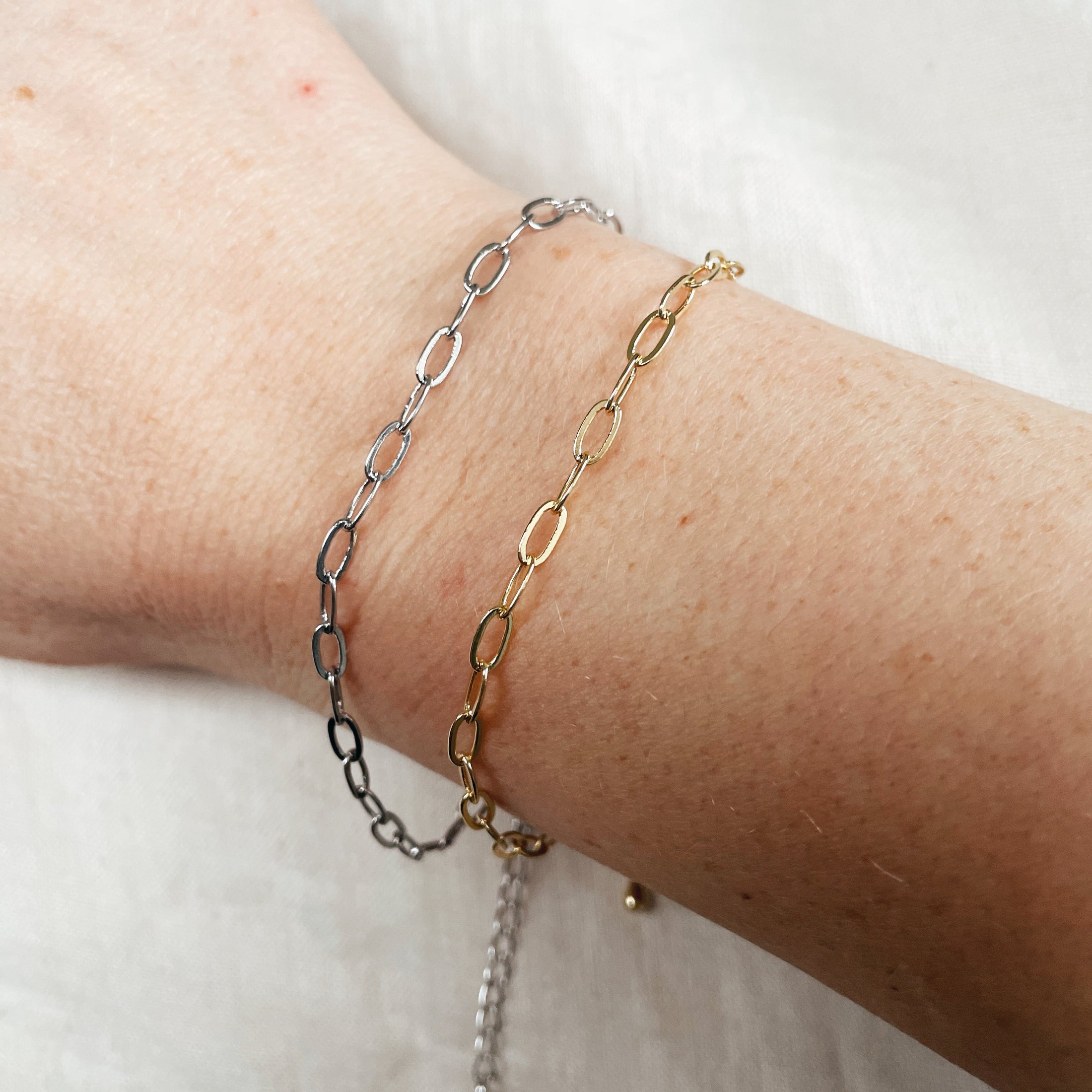 Two chain bracelets on a wrist against a white background
